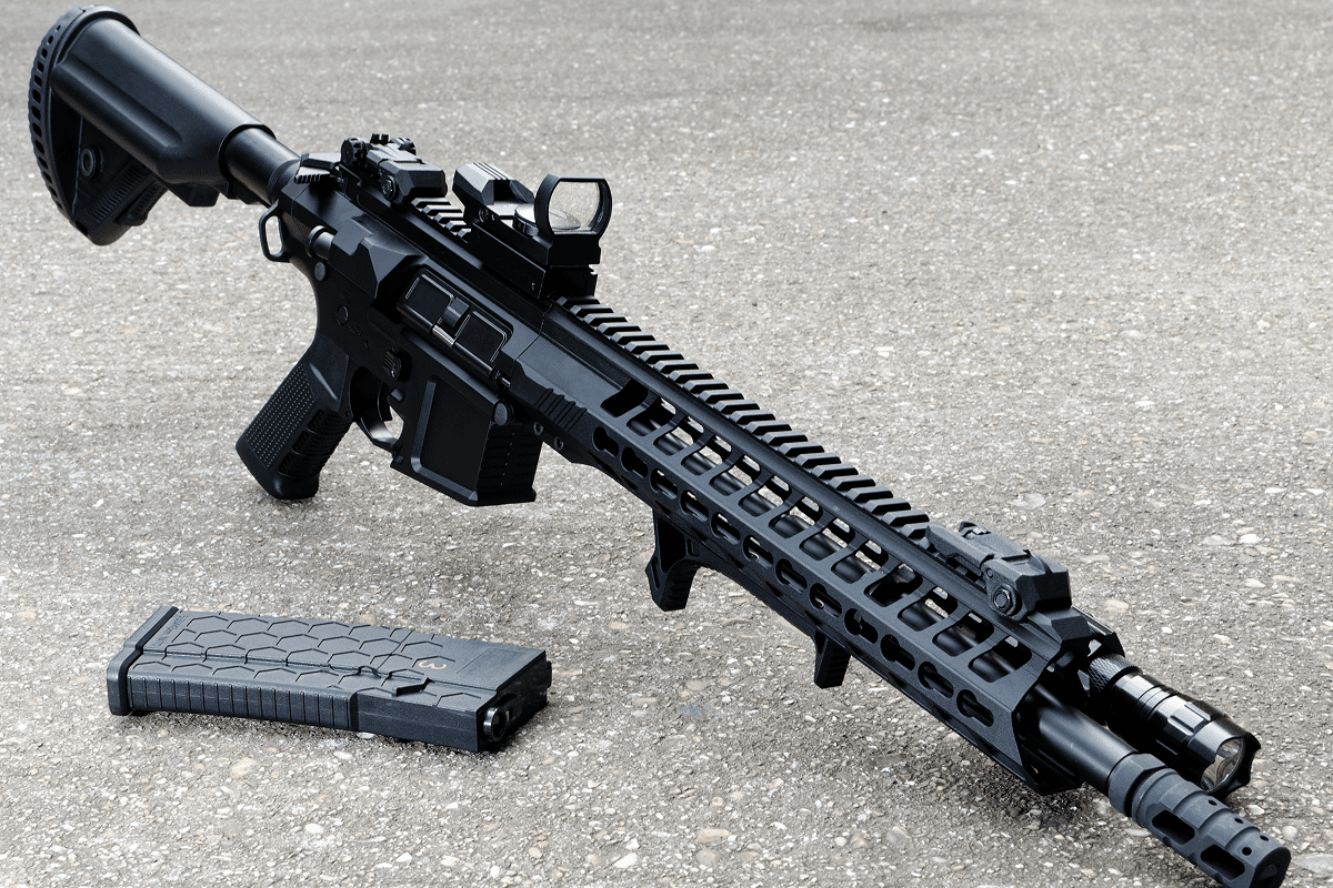 Black rifle with magazine on concrete surface.