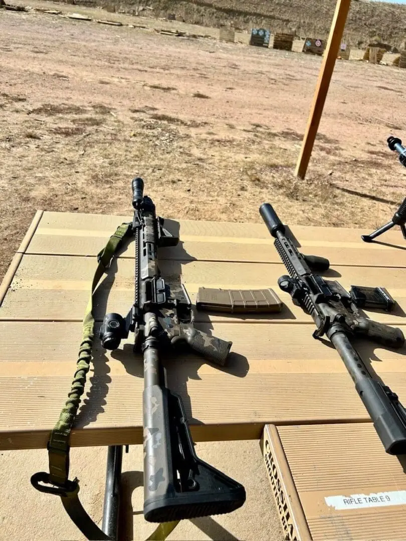 Two rifles with scopes resting on wooden pallets in a desert setting.