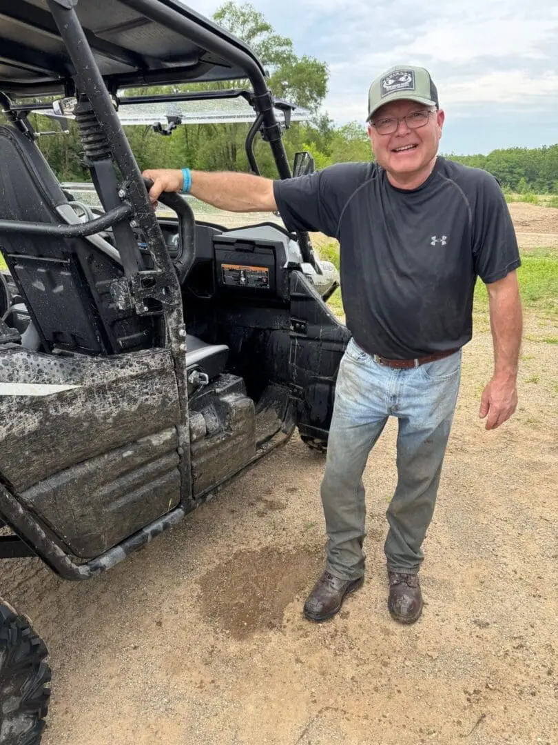 Man standing next to a muddy off-road vehicle in outdoor setting.