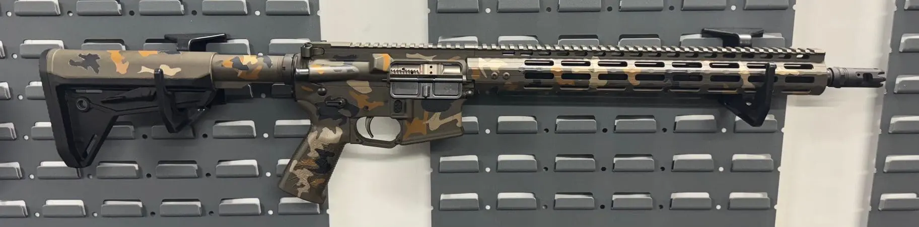 Close-up of a camouflaged rifle on a gray panel background.