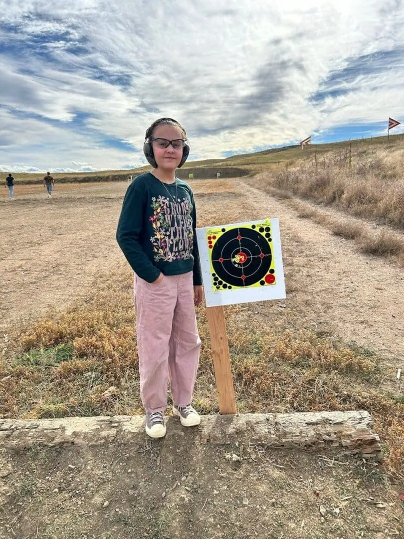 A young person stands beside a target board in an outdoor field.