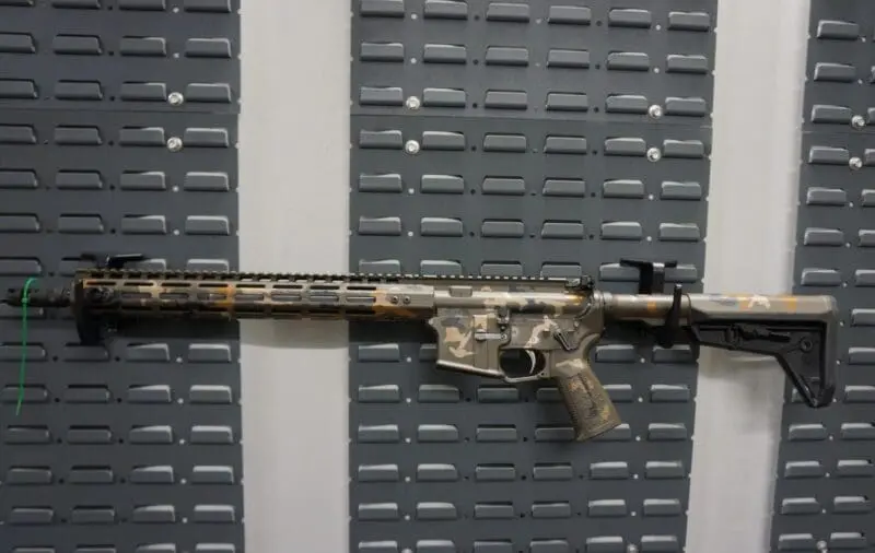 A camouflaged rifle displayed on a textured gray surface.