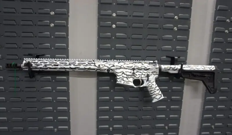 A camouflaged rifle displayed on a textured background.