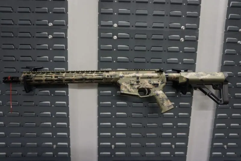 A camouflaged assault rifle displayed vertically on a wall.