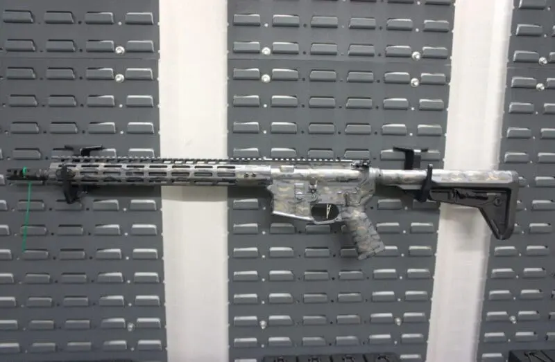 A modern rifle with a long barrel and scope mounted on a wall.