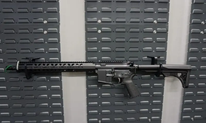 A tactical rifle mounted on a wall with a gray panel background.