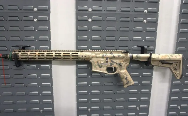 Camouflaged rifle on display against a gray background.