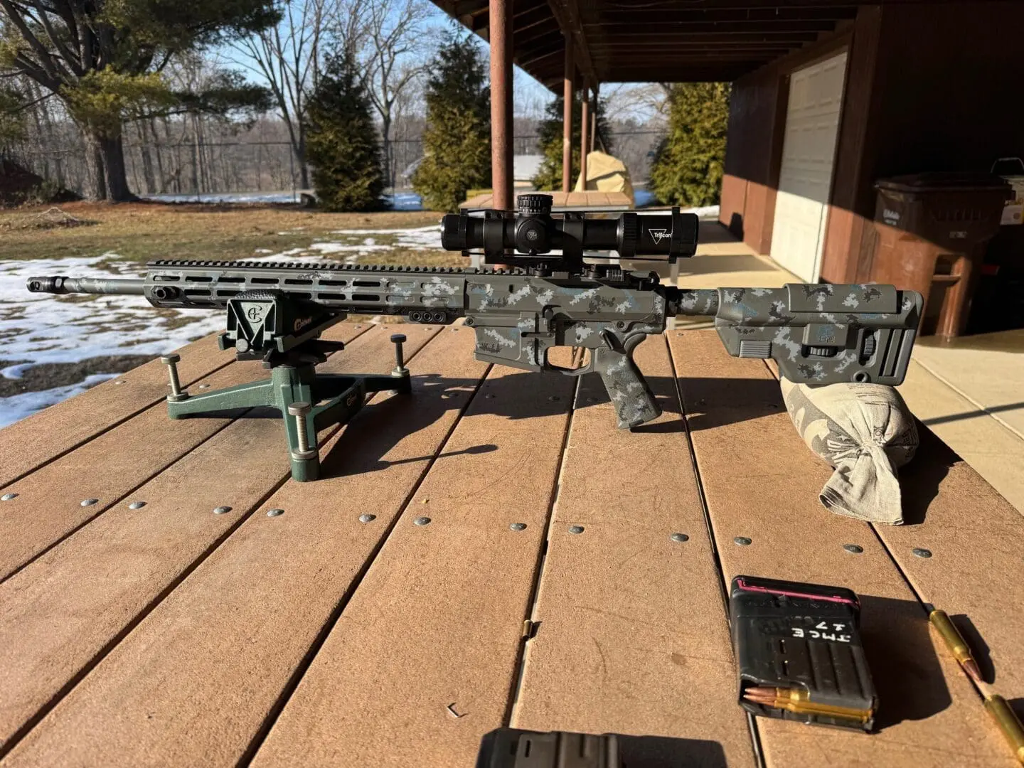 Camouflaged precision rifle and magazine on bench