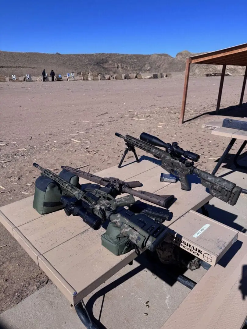 Camouflaged precision rifles on outdoor shooting bench