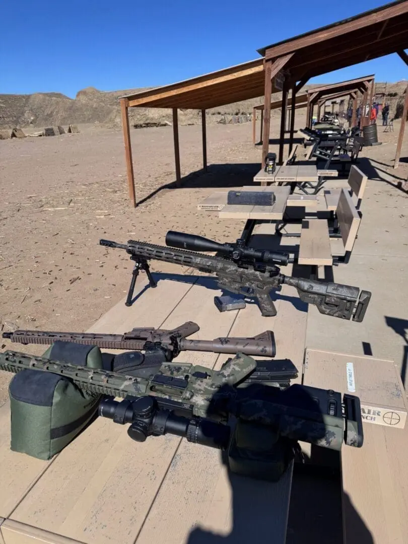 Camouflaged precision rifles on outdoor shooting benches