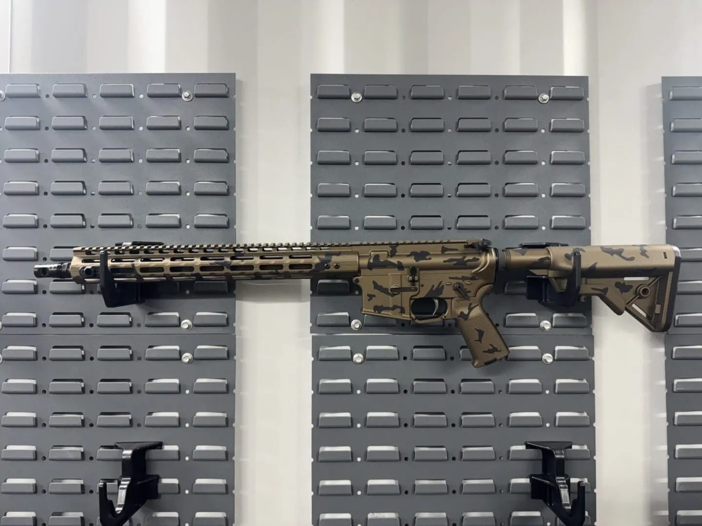 Desert camo AR-style rifle mounted on pegboard