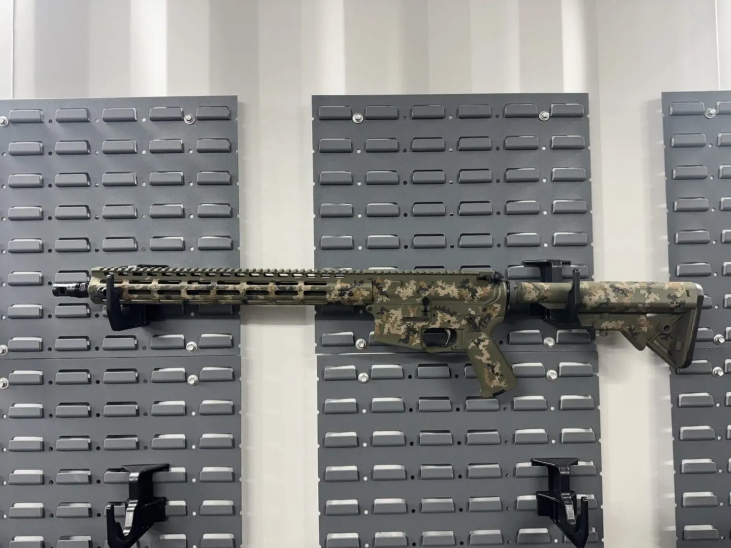 Camouflage AR-style rifle mounted on display wall