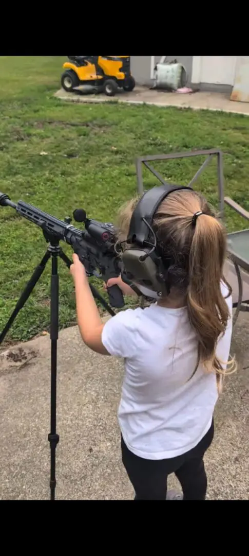 Child wearing hearing protection aiming rifle outdoors