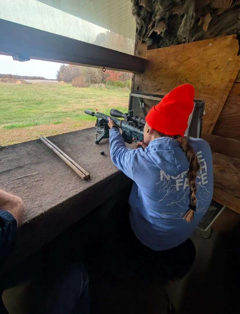 Person aiming scoped rifle from hunting blind