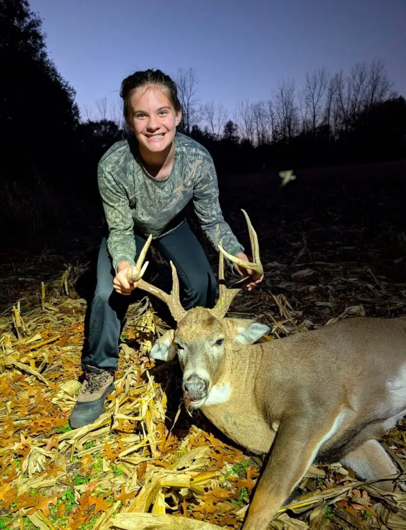 Smiling person posing with buck at dusk